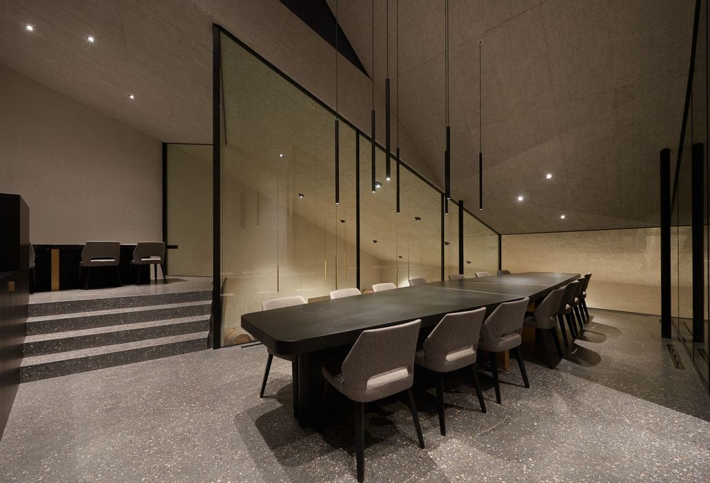 Ein minimalistischer Konferenzraum mit einem langen schwarzen Tisch, grauen Stühlen und einer Glaswand, hinter der Weinfässer zu sehen sind.