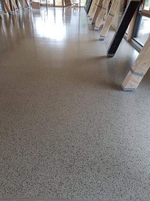 Ein frisch geschliffener und versiegelter Terrazzoboden in einer hellen Halle, an deren Rand Holzgestelle und Materialien gelagert sind.
