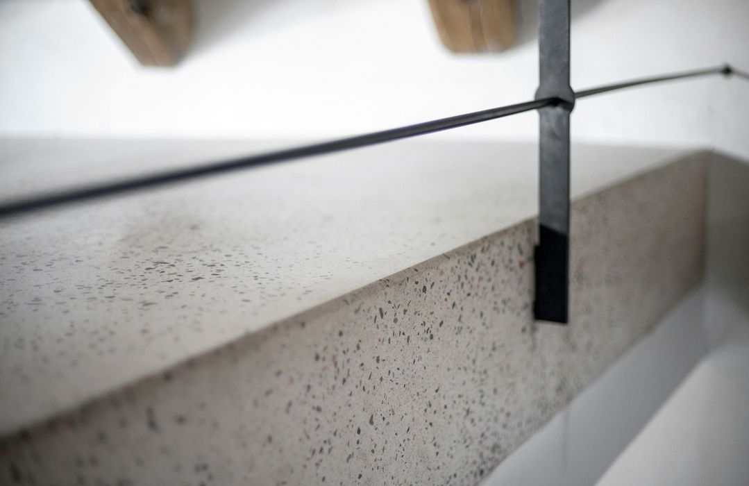 Nahaufnahme einer Treppenstufe aus hellem Terrazzo mit einem vertikalen schwarzen Metallgeländer-Element.