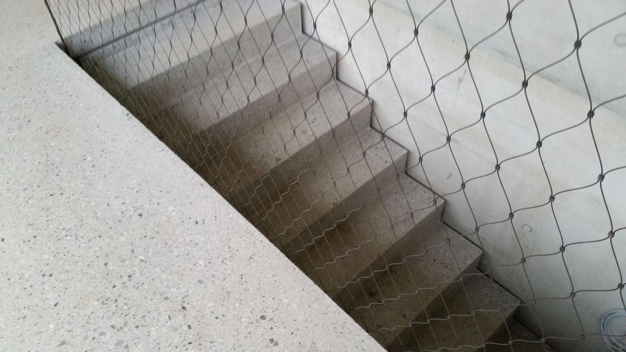 Eine Treppe aus hellem Beton, die hinter einem metallischen Drahtnetz verläuft.