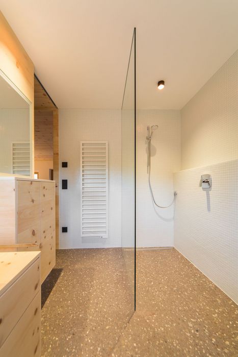 Ein modernes Badezimmer mit einer bodenebenen Dusche, die durch eine Glaswand abgetrennt ist, inklusive weißen Mosaikfliesen und hellen Holzfronten.
