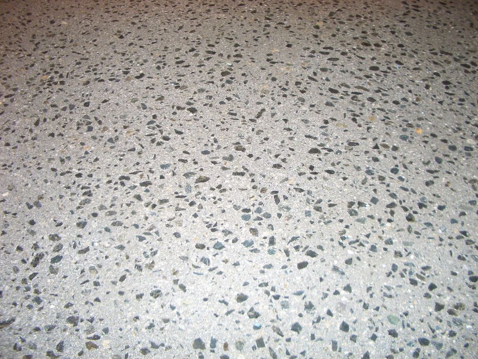 Nahaufnahme eines Terrazzo-Bodens mit einer hellgrauen Betonoberfläche, die mit vielen dunklen, unregelmäßigen Steingranulaten durchsetzt ist.
