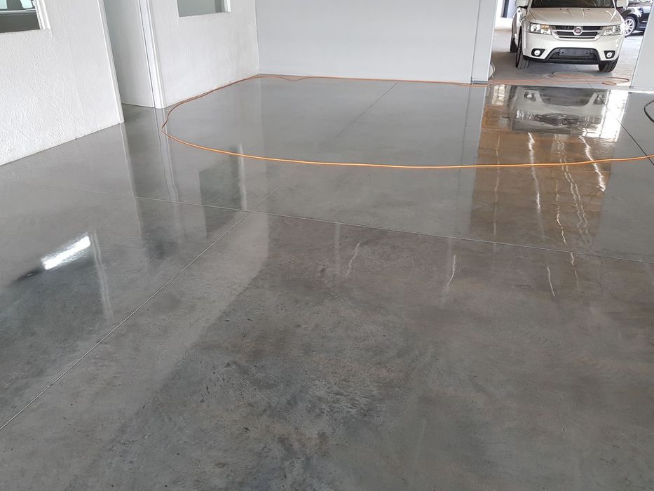 Ein frisch versiegelter, glänzender Betonboden in einer Garage mit einem weißen Auto im Hintergrund.