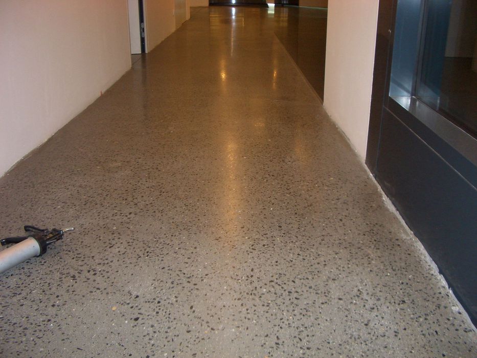 Ein langer, leerer Flur mit einem polierten, grauen Betonboden, auf dem links vorne eine Silikonspritze liegt.