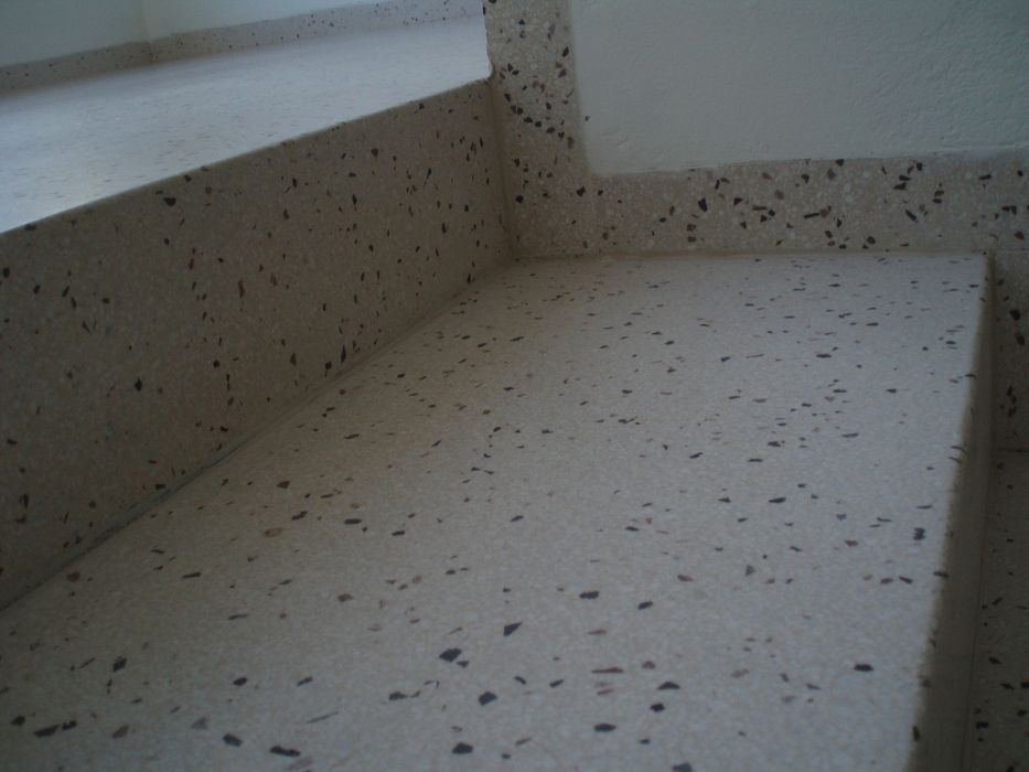 Nahaufnahme einer Treppenstufe mit beigefarbenem Terrazzo-Belag und gesprenkelten dunklen Steinchen.