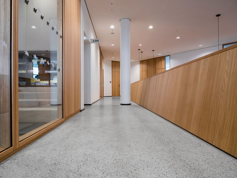 Ein heller, moderner Flur mit grau gesprenkeltem Boden und Holzwandverkleidungen, der in der Mitte von einer weißen Säule unterbrochen wird.