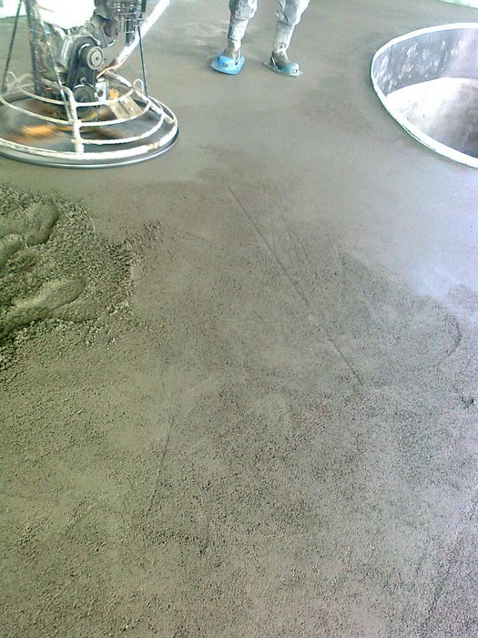 Ein Bauarbeiter bei der Arbeit mit einem elektrischen Betonglätter auf einer Betonfläche neben einer Aussparung im Boden.