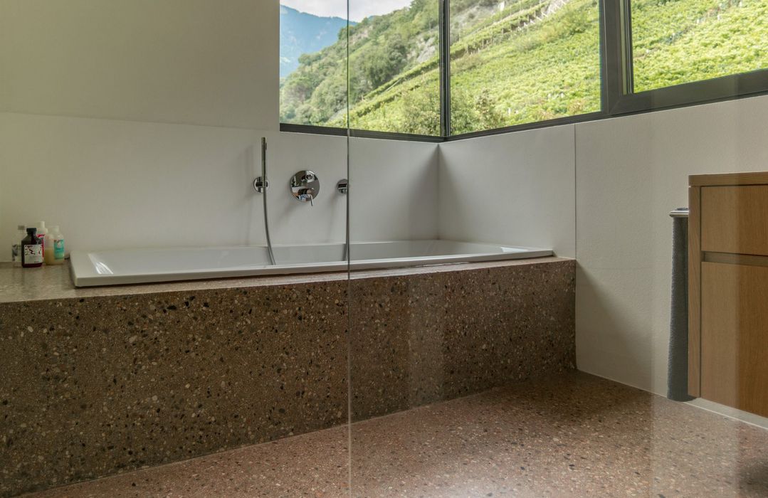 Eine Badewanne mit einer Verkleidung aus Terrazzo vor einem großen Fenster mit Blick auf eine Weinbergslandschaft.