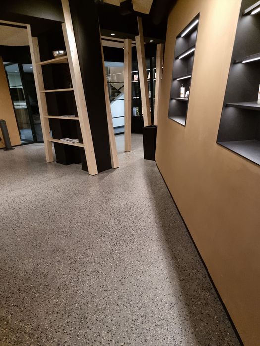 Ein moderner Innenraum mit einem Boden aus gesprenkeltem Terrazzo, schwarzen Wänden und holzfarbenen, beleuchteten Wandregalen.