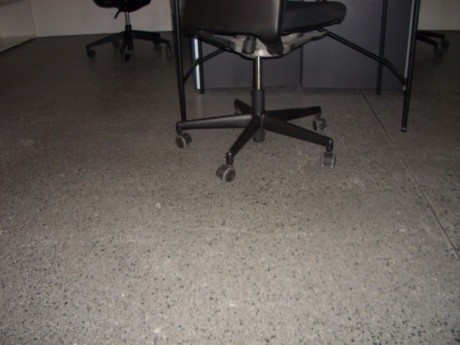 Ein schwarzer Bürostuhl auf einem dunklen, gesprenkelten Boden in einem Büro.