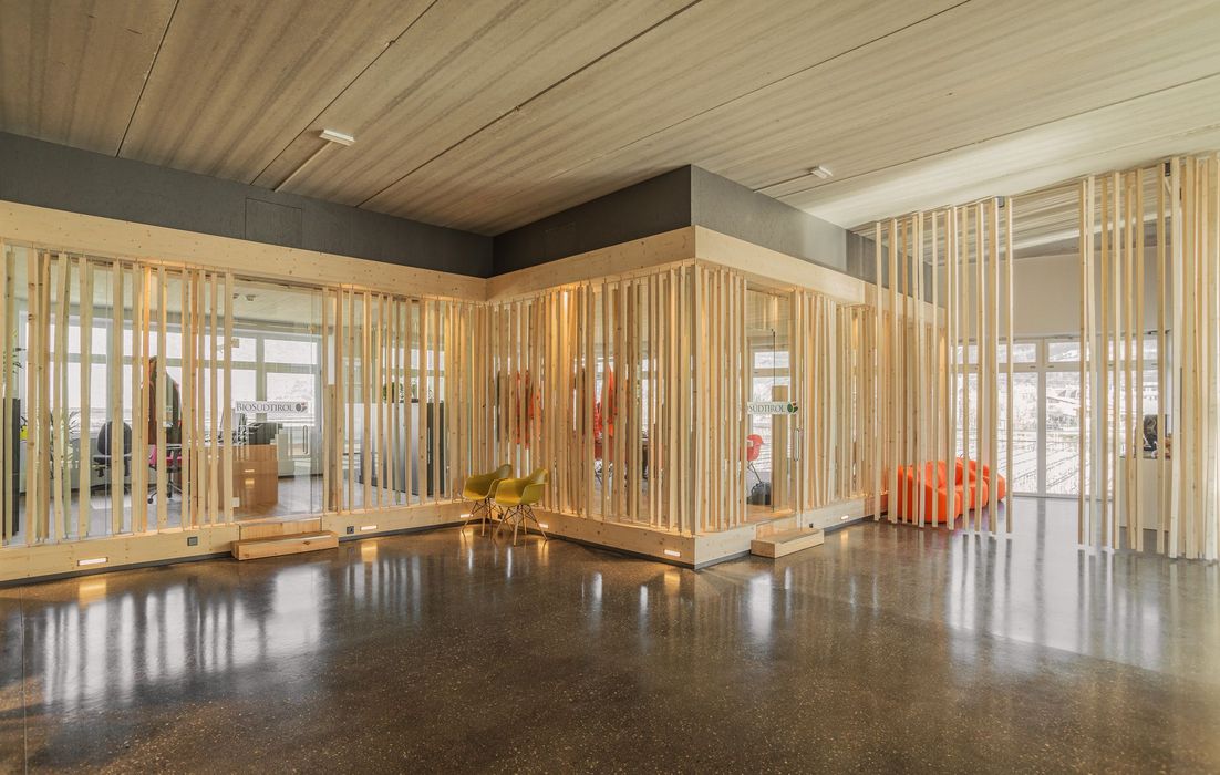 Ein minimalistisch gestaltetes Bürogebäude mit gläsernen Trennwänden, die von vertikalen Holzlamellen eingerahmt sind, und einem polierten Betonboden.