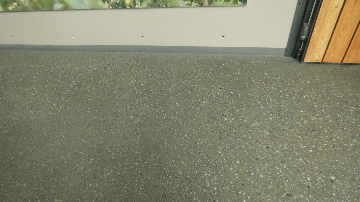 Ein gesprenkelter Terrazzo-Boden vor einer hellen Wand mit einer Holztür in der Ecke.