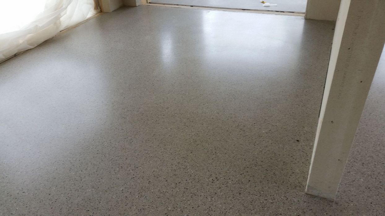 Ein frisch fertiggestellter, grauer Sichtestrichboden in einem Innenraum mit einer weißen Wandstruktur am rechten Bildrand.