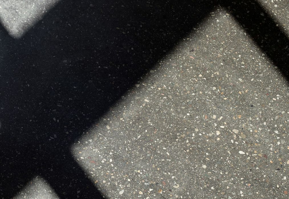 Eine Nahaufnahme von grauem Terrazzo-Boden mit scharf abgegrenzten, dunklen Schattenwürfen auf der Oberfläche.