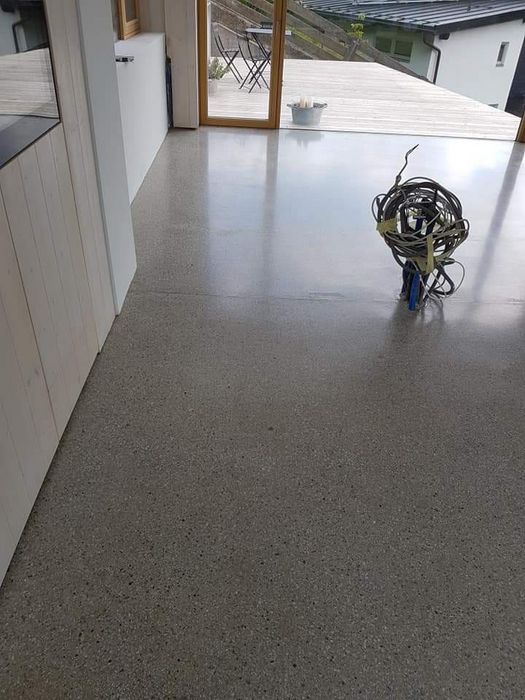 Ein glatter, polierter Betonboden in einem modernen Innenraum, der zu einer Außenterrasse führt, mit einem Kabelbündel, das aus dem Boden ragt.