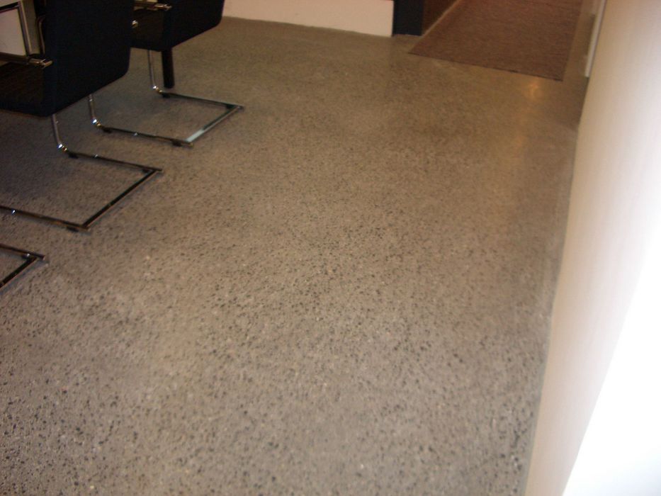 Ein glatter, grauer Betonboden in einem Innenraum mit zwei Stühlen, deren Beine ebenfalls in der Ansicht enthalten sind.