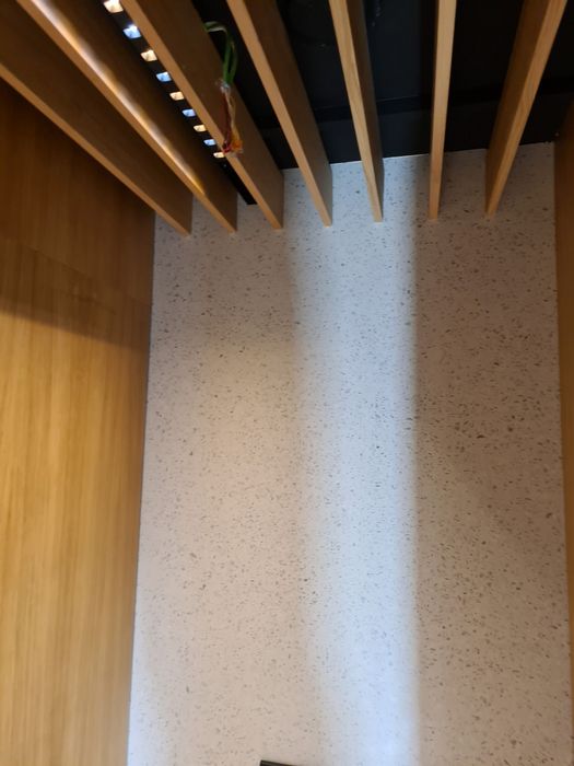 Innenansicht einer Wandverkleidung mit einer hellgrauen Steinwand in Sprenkeloptik, eingerahmt von vertikalen Holzelementen und einer hängenden Deckenleuchte.