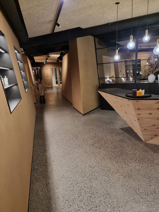 Innenansicht eines modernen Spa- oder Wellnessbereichs mit Empfangstheke in Holzoptik, dunkler Glaswand und einem Flur mit indirekter Beleuchtung.