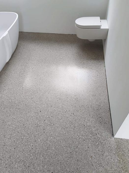 Badezimmer mit weißer Badewanne, wandhängender Toilette und einem grauen Terrazzoboden.