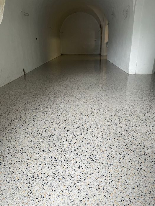 Ein renovierter Raum mit einem hellen Terrazzoboden und glatten weißen Wänden unter einem Gewölbebogen.