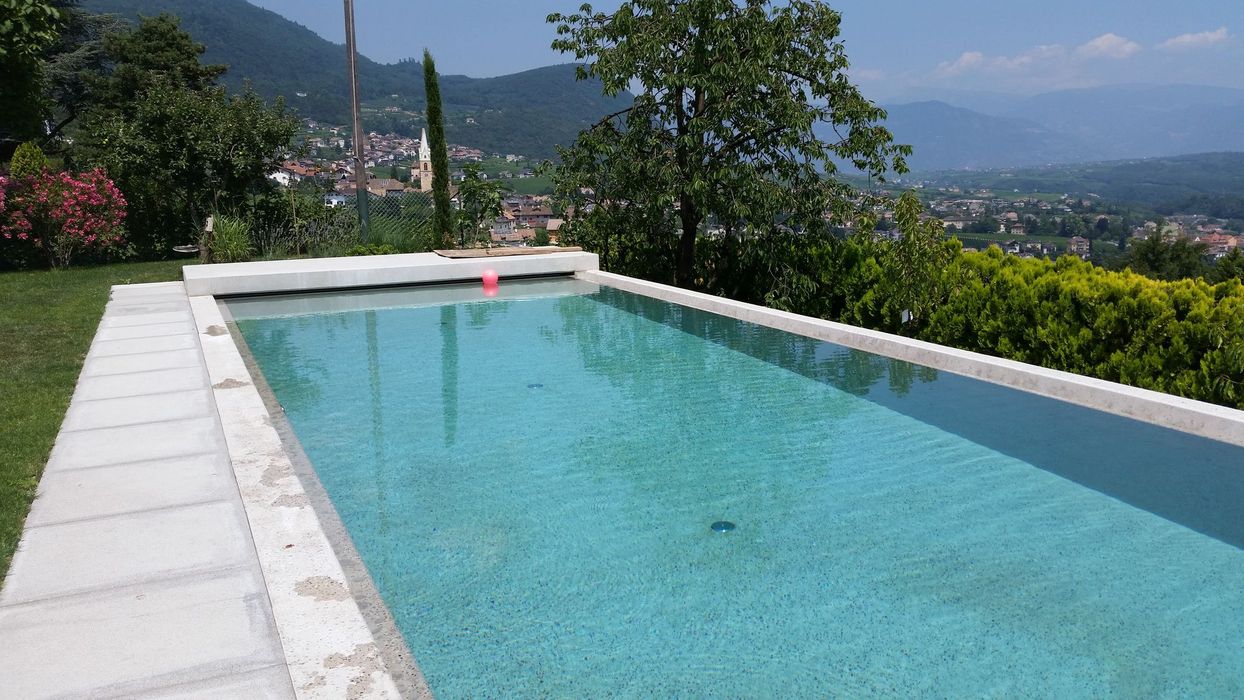 Ein rechteckiger Swimmingpool mit türkisfarbenem Wasser im Garten vor der Kulisse von grünen Hügeln und einer Ortschaft.