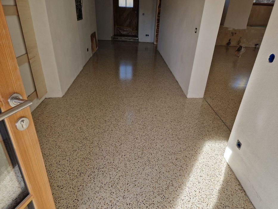 Ein renovierter Flur mit einem glatten, gesprenkelten Terrazzoboden und weißen Wänden während der Bauphase.