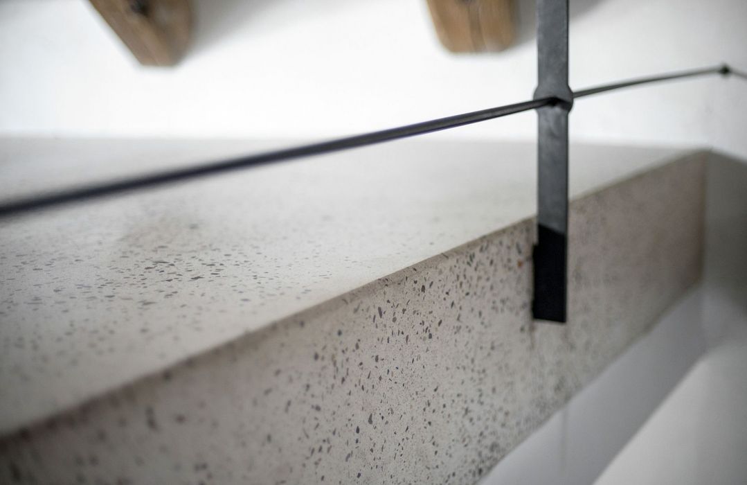 Nahaufnahme einer Terrazzotreppenstufe mit einem schwarzen Metallgeländer in einem minimalistischen Innenraum.