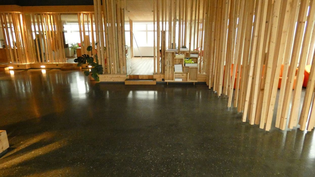 Ein geräumiger Innenraum mit poliertem dunklem Betonboden und einer Raumtrennung aus vertikalen Holzlatten, die den Bereich in Zonen unterteilt.