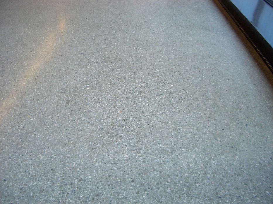Eine Nahaufnahme eines glatten, grauen Terrazzo-Bodens mit feiner Körnung, teilweise beleuchtet durch seitliches Licht.