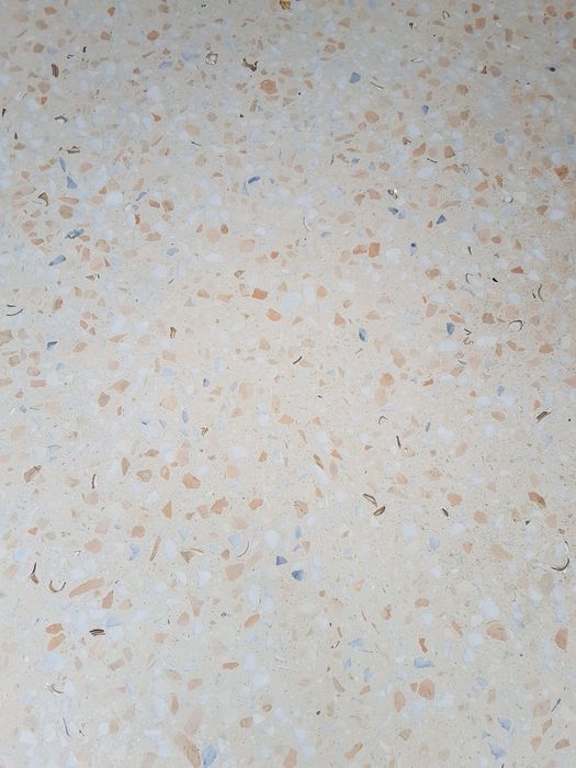 Eine Nahaufnahme einer hellbeigen Terrazzofläche mit eingestreuten kleinen Steinpartikeln und Muschelfragmenten.