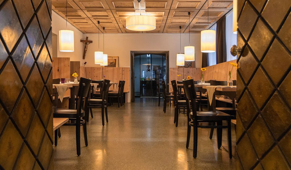 Ein gemütlicher Gastraum mit Holztischen, dunklen Stühlen, einer Kassettendecke und warmem Pendelleuchtlicht.