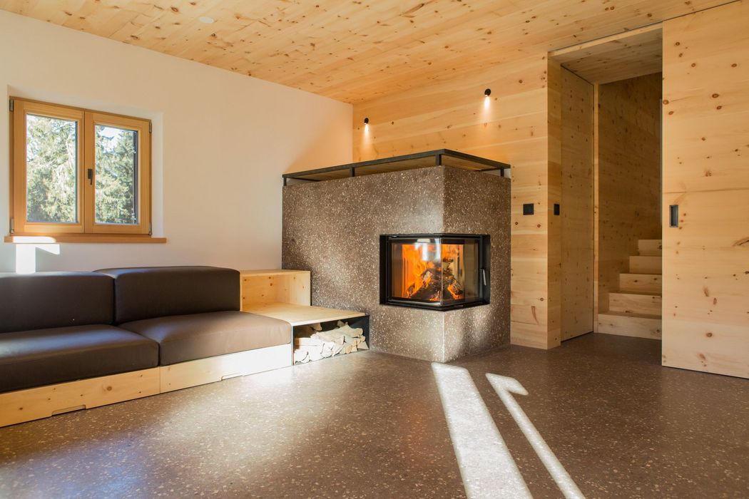 Ein minimalistisch eingerichteter Wohnraum mit einem modernen Eckkamin, einem dunkelgrauen Sofa mit integriertem Holzregal und holzverkleideten Wänden und Decken.