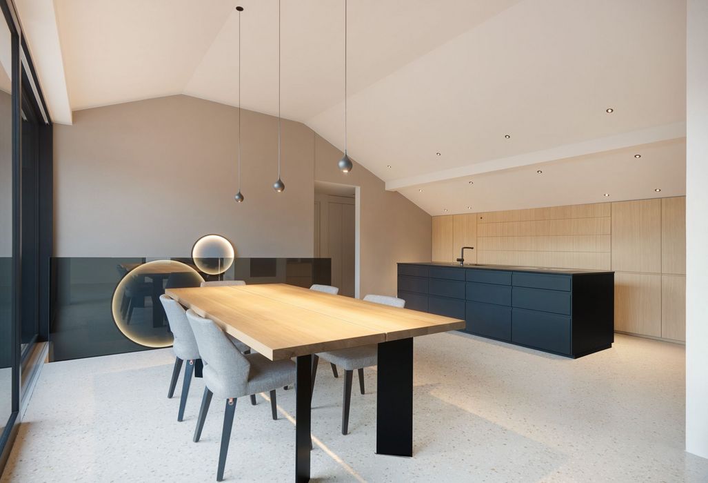 Ein minimalistischer Essbereich mit einem langen Holztisch, hellgrauen Stühlen und einer dunklen Kücheninsel im Hintergrund in einem modernen Raum mit schrägen Decken.