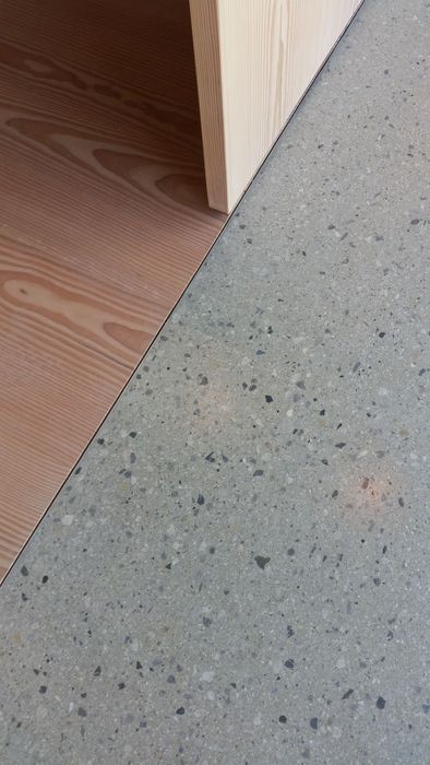 Ein Nahaufnahme-Bild zeigt den Übergang zwischen einer glatten Betonfläche und einer Oberfläche aus hellem Kiefernholz.