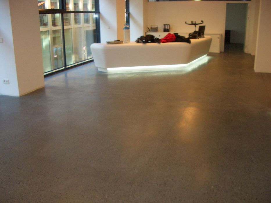 Ein heller Empfangstresen aus weißem Material mit indirekter Beleuchtung steht in einem Büro mit glattem Betonboden und großen Fensterfronten.