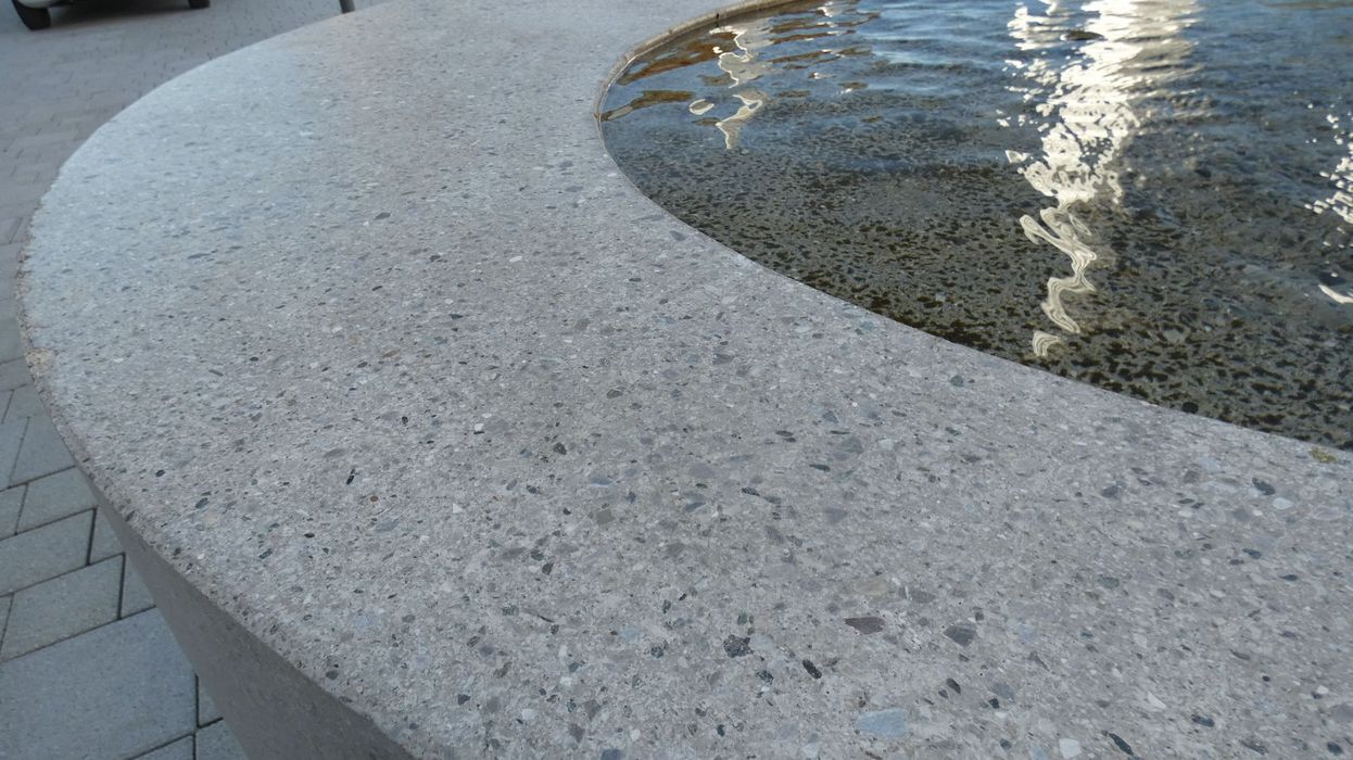 Ein Nahaufnahme-Ausschnitt eines runden Brunnenbeckens aus hellem Terrazzo-Stein im Außenbereich.