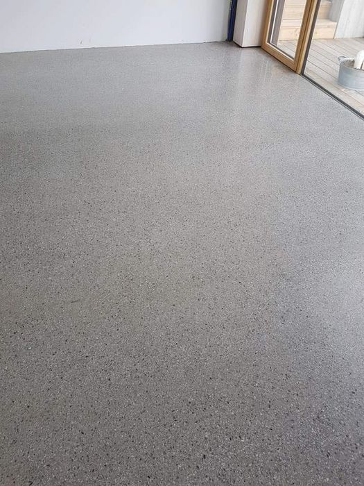 Ein glatter, hellgrauer Betonboden mit feiner Sprenkelung in einem Innenraum, angrenzend an eine Terrasse mit Glasfront.