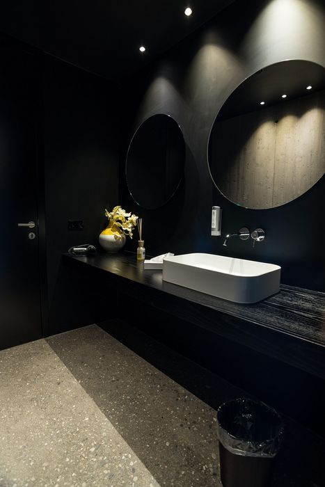 Modernes Badezimmer mit schwarzem Waschtisch, weißem Aufsatzwaschbecken, zwei runden Spiegeln und dezenter Beleuchtung.