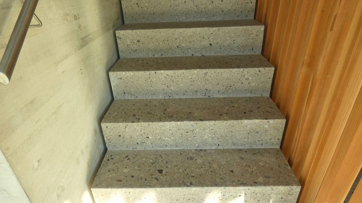 Eine Treppe aus grauem Terrazzo mit einer linken Betonwand und einer rechten Holzwand.