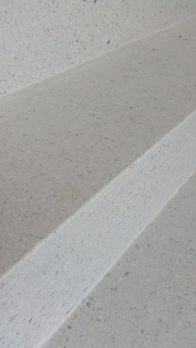Nahaufnahme einer Treppenstufe aus hellgrauem Terrazzo mit gesprenkelter Textur.
