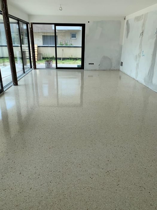 Ein frisch verlegter, hochglänzender Terrazzoboden in einem noch im Umbau befindlichen Wohnraum mit großen Terrassenfenstern.