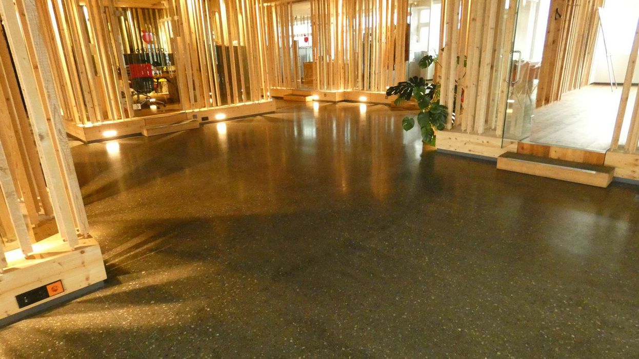 Ein glatt polierter Betonboden in einem modernen Bürogebäude, umgeben von vertikal verlaufenden Holzlattung-Elementen.