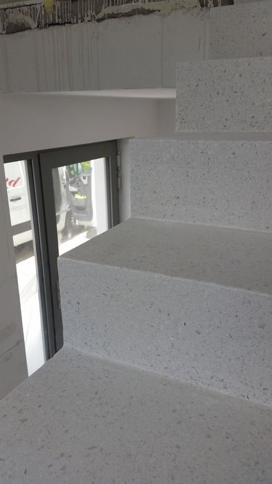 Eine Nahaufnahme einer hellen Treppe aus Terrazzo-Material in einem Rohbau mit einem sichtbaren Fenster im Hintergrund.