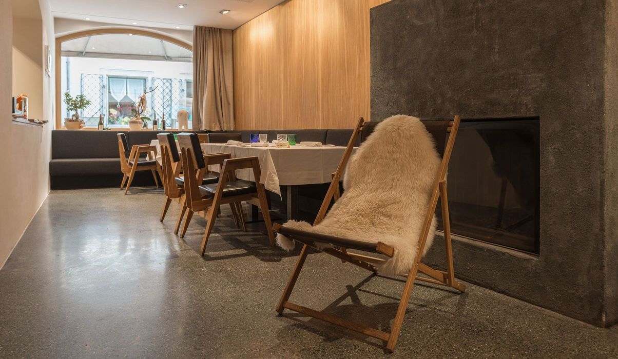 Ein Restaurant-Innenraum mit einem hellen Fell auf einem Holzgestell im Vordergrund, Tischen und Stühlen im Hintergrund sowie einer dunklen Kaminwand.
